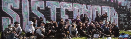Eine Gruppe junger FLINTA* vor einem großen Sisterhood-Graffitti
